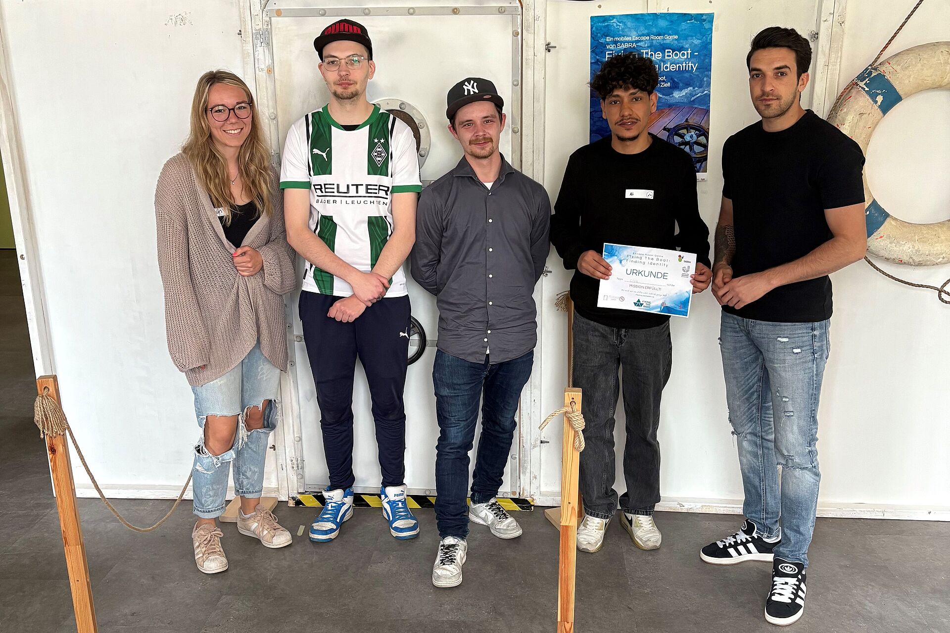 Eine Frau und vier Jugendliche Männer vor einer Wand.