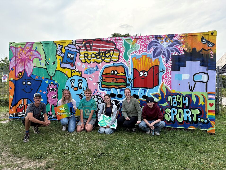 Junge Menschen vor einer besprayten bunten Wand.