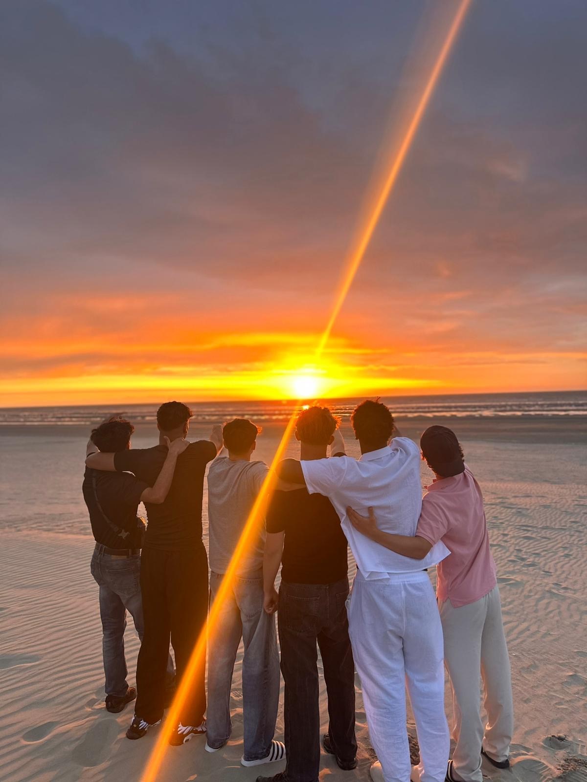 Mehrere Jugendliche umarmen sich und schauen einen Sonnenuntergrang am Strand an.